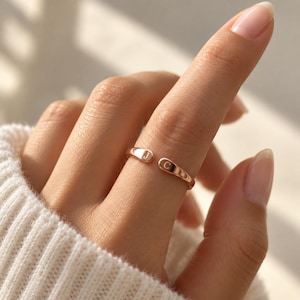 May include: A rose gold open-style ring featuring two rounded ends, each engraved with a single uppercase letter. One end displays the letter J, and the other end displays the letter C. The band has a smooth, polished finish and a simple design.