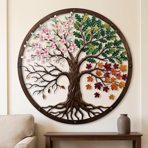 May include: A circular metal wall art piece featuring a tree with four distinct seasonal sections. The top left shows pink spring blossoms, the top right displays green summer leaves, the bottom right has autumn foliage, and the bottom left shows bare winter branches.