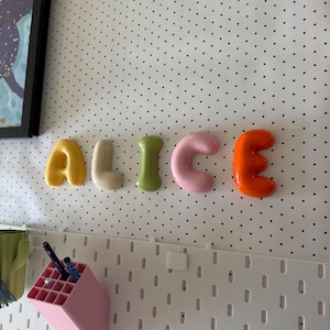 May include: Five individual, rounded, three-dimensional letters spelling the name ALICE. Each letter features a smooth, glossy finish in a distinct color: yellow for A, beige for L, light green for I, soft pink for C, and bright orange for E.