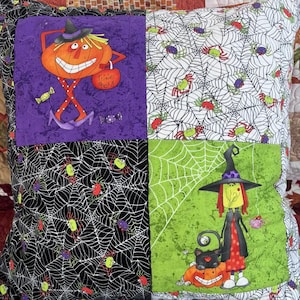May include: A square decorative cushion featuring a four-panel patchwork design with Halloween themes. Panels include a pumpkin character with a witch hat holding a bag labelled Trixie Treats, spider webs with colourful spiders, and a witch.