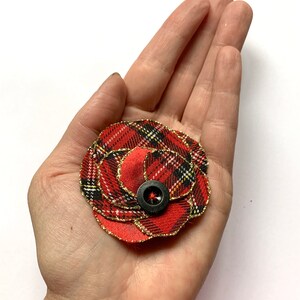 May include: A red and black plaid fabric flower with gold glitter trim and a black button in the center.