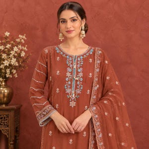May include: A rust-coloured long-sleeved tunic featuring intricate floral embroidery in shades of light blue, white, and pink around the neckline and cuffs. The garment includes silver sequin detailing on the sleeves and a matching sheer dupatta.