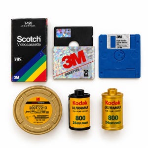 May include: A collection of vintage media including a Scotch T-120 VHS videocassette, a 3M diskette box with holographic packaging, a blue 3M high density diskette, a round gold Kodak Vision3 film canister, and two yellow Kodak Ultramax 800 film rolls.