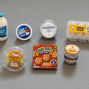 May include: A collection of miniature food items including a bottle of Fresh Milk, a tub of Cool Whip, a container of Philadelphia cream cheese, a carton of Fresh Eggs, a plastic Fruit Tray, a box of Bagel Bites, and a small glass Oats Jar.