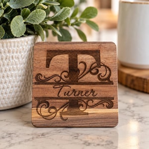 May include: A square wooden coaster featuring a dark brown laser-engraved design. The center displays a large capital letter T with the name Turner written in cursive script across the middle, surrounded by decorative scrollwork patterns.