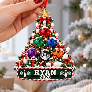 Op de afbeelding: Een kerstboomvormig ornament met kleurrijke bowlingballen en witte kegels tussen groene takken, bekroond met een gouden ster. Een rechthoekige basis aan de onderkant toont de naam RYAN en het jaartal 2026 in witte letters.