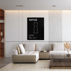 May include: A black rectangular poster featuring the white text SOYUZ at the top, a white outline illustration of a spacecraft in the center, and technical text at the bottom including SOYUZ PROGRAM, displayed in a black frame on a white wall.