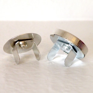 May include: Two silver magnetic closures for sewing projects. The closures are round and have a metal loop on the back.
