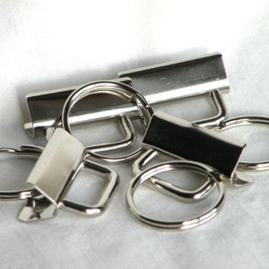 May include: A collection of silver-toned metal key rings and key chain attachments. The key rings are round and oval shaped. The key chain attachments are rectangular and have a D-ring.