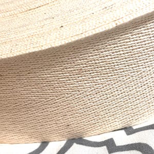 May include: Close-up of a natural beige cotton webbing, showing the woven texture of the fabric.