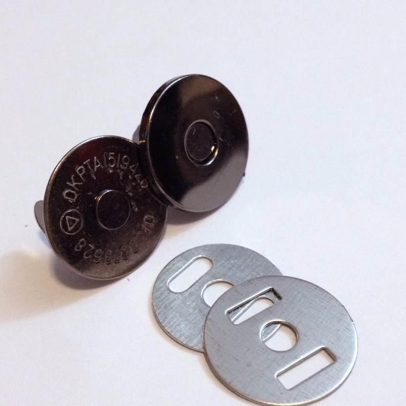 May include: Two silver magnetic closures with a black finish and a silver metal plate with a hole in the center. The magnetic closures have a circular shape and are marked with the text "DKPTA151944".