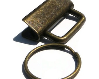Könnte beinhalten: Ein bronzefarbener Schlüsselring aus Metall mit einer rechteckigen Schlaufe und einem runden Ring. Die Schlaufe hat an einer Seite eine kleine Öffnung.