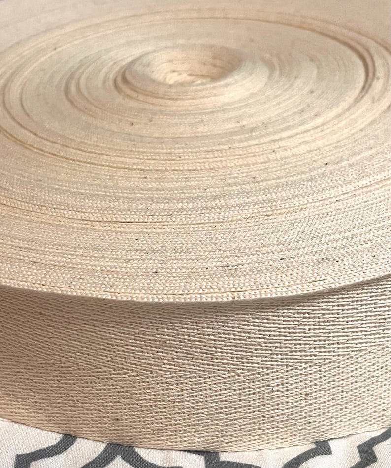 May include: A close-up of a roll of natural cotton twill tape. The tape is tightly wound and has a smooth, even texture.