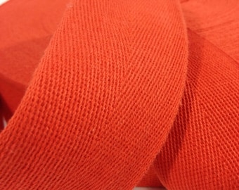 May include: A roll of bright orange cotton twill tape. The tape is woven with a diagonal pattern and has a smooth, slightly textured surface.
