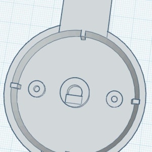 May include: A light grey circular mechanical component featuring a central circular cutout with a small padlock icon, two smaller circular holes on either side, and a rectangular tab extending from the top edge of the outer rim.