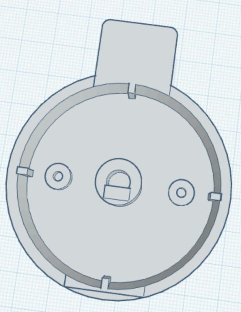 May include: A light grey circular mechanical component featuring a central circular cutout with a small padlock icon, two smaller circular holes on either side, and a rectangular tab extending from the top edge of the outer rim.