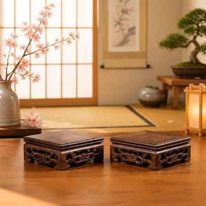 May include: Two square wooden display stands featuring intricate openwork carvings along the sides. Each stand has a flat, smooth top surface and a dark brown finish, designed to elevate small decorative objects with a stable, elevated base.