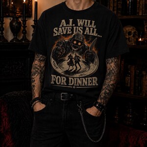 May include: A black short-sleeve t-shirt featuring a graphic print of a robotic figure holding a fork and knife over a plate with two small human silhouettes. The text reads A.I. WILL SAVE US ALL... FOR DINNER in a distressed, vintage-style font.