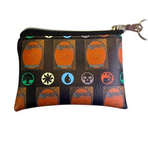 May include: A black zippered pouch featuring a repeating pattern of Magic: The Gathering card backs and mana symbols. The pouch has a silver zipper and a small key ring attached. The overall design is a nod to the popular trading card game.