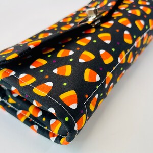 May include: A black fabric wallet with a candy corn pattern. The wallet has a silver clasp and is folded closed.