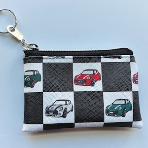 May include: A black and white checkered coin purse with a silver key chain. The purse has a checkered pattern with four mini cooper cars printed on it. The cars are red, green, white, and blue.