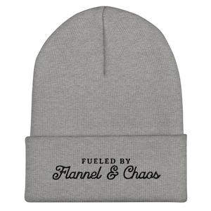 Może przedstawiać: Szara melanżowa czapka typu beanie z wywinięciem i czarnym haftowanym napisem z przodu o treści FUELED BY Flannel & Chaos. Dzianinowa czapka ma prążkowaną fakturę, zaokrągloną górę oraz wywinięty brzeg wykonany z miękkiego materiału.