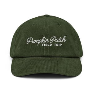 May include: A dark olive green corduroy baseball cap featuring the white embroidered text Pumpkin Patch FIELD TRIP centred on the front panel. The hat has a structured crown, a curved brim, and a fabric strap closure at the back.