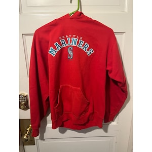 May include: Red hooded sweatshirt with the Seattle Mariners logo in blue and white on the back. The logo says "Seattle Mariners" with a stylized "S" in the center.