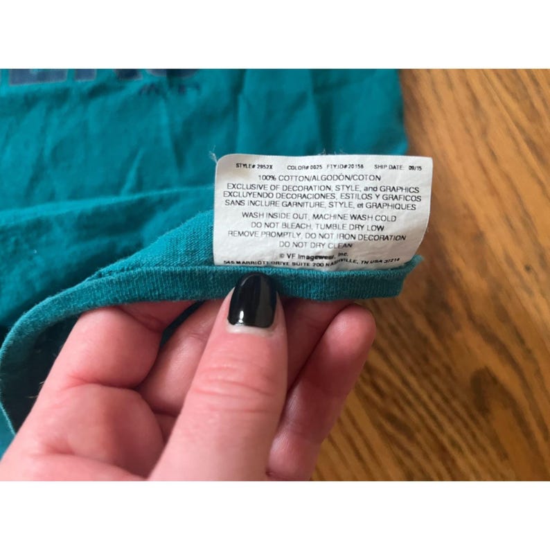 May include: A teal blue t-shirt with a white tag that reads "STYLE 29538 COLOR 2825 FY1020158 SSP DATE 38/15 100% COTTON/ALGODON/COTON EXCLUSIVE OF DECORATION, STYLE, and GRAPHICS EXCLUYENDO DECORACIONES, ESTILOS Y GRAFICOS SANS INCLURE GARNITURE STYLE, et GRAPHIQUES WASH INSIDE OUT, MACHINE WASH COLD DO NOT BLEACH, TUMBLE DRY LOW REMOVE PROMPTLY, DO NOT IRON DECORATION DO NOT DRY CLEAN VF Imagewear SAS MARRIOTEORIVE SUITE 200 NASHVILLE, TN 37214 USA"