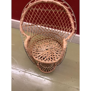 Puede incluir: Una pequeña silla de mimbre tejida con diseño de pavo real. La silla tiene respaldo redondeado y asiento circular. Los bordes de la silla están adornados con rayas blancas y negras. La silla está hecha de mimbre de color natural.