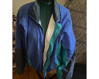 May include: A blue, green, and black windbreaker jacket with a zipper closure. The jacket has a white lining and a drawstring hood.