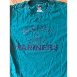May include: A teal blue t-shirt with the text "Seattle Mariners Established 1977" in navy blue lettering.