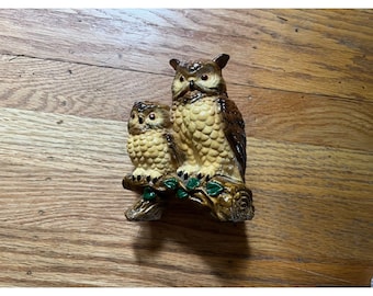 May include: A ceramic owl figurine with a smaller owl perched on a branch. The owls are painted in shades of brown, tan, and green.