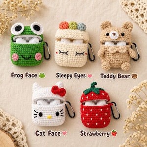 Puede incluir: Cinco fundas de ganchillo para auriculares con forma de rana verde, una funda color crema con ojos dormilones y pompones de colores, un oso de peluche beige, una cara de gato blanca con lazo rojo y una fresa roja, cada una con un mosquetón.