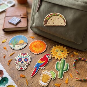 May include: A collection of embroidered patches featuring a taco, a desert landscape with a cactus and sun, an orange marigold flower, a sugar skull, a red and blue parrot, a sun face, a green cactus, and a glass of tequila with a lime wedge.