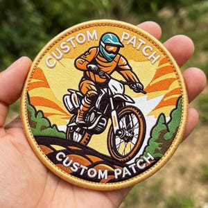 May include: A circular embroidered patch featuring a motocross rider on a dirt bike. The design includes a yellow sunburst background, green trees, and the text CUSTOM PATCH in white letters at the top and bottom of the border.