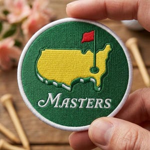 May include: A circular embroidered patch featuring a yellow map of the United States on a dark green background. A red golf flag is positioned on the map. The word Masters is embroidered in white cursive script at the bottom of the patch.