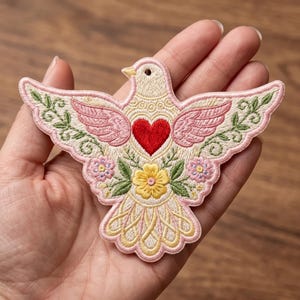 May include: An embroidered patch shaped like a dove with cream-colored thread, featuring a bright red heart on its chest, pink wing accents, a yellow flower at the center, and green leafy vine details along the wings, finished with a pink border.