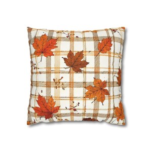 May include: A square throw cushion featuring a cream-coloured fabric base with a brown and tan plaid pattern. The surface is decorated with scattered, detailed illustrations of orange and red maple leaves across the entire front side.