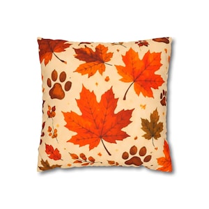 May include: A square throw cushion featuring a cream-coloured background with a repeating pattern of vibrant orange and red maple leaves, small brown paw prints, and delicate sprigs of berries scattered across the entire surface of the fabric.