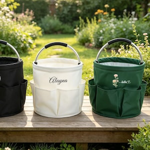 Può includere: Tre borse da giardino cilindriche con manici in metallo e impugnature nere. La borsa nera presenta il testo YOUR LOGO, quella bianca mostra il nome Alayna e quella verde un motivo floreale con il nome Katie e un simbolo a forma di cuore.