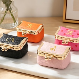 May include: Four small, rectangular coin purses with gold-toned metal kiss-lock clasps. One is black with the gold letter A, one is orange with the letter R, one is hot pink with red polka dots and the letter H, and one is light pink with the letter A.
