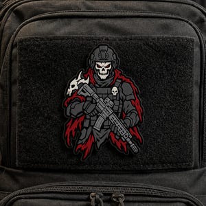 May include: A tactical morale patch featuring a skull-faced soldier wearing a helmet and dark armor, holding a rifle. The figure is draped in a tattered red cape and accented with small skull motifs on the shoulder and chest, set against a black background.