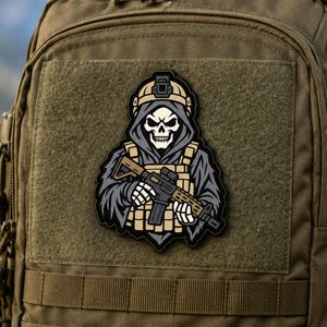 May include: A tactical morale patch featuring a hooded skeleton figure wearing a tan combat helmet and vest, holding a rifle. The design uses a colour palette of tan, grey, black, and white, and is attached to the front of a tan tactical backpack.