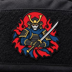 Könnte beinhalten: Ein schwarz-rot-blaues PVC-Aufnäher-Abzeichen mit einem stilisierten Samurai-Krieger in traditioneller Rüstung und Helm, der ein Katana-Schwert hält. Die Figur ist vor einem Hintergrund aus leuchtend roten Flammen auf schwarzem Stoff platziert.