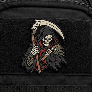 May include: A black tactical patch featuring a grim reaper character with a white skull, red hood lining, and a large scythe. The figure wears dark, tattered clothing with brown straps and armor details, attached to a black fabric surface.