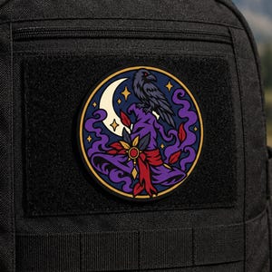 Può includere: Una toppa circolare fissata su uno zaino nero con un'illustrazione grafica di un corvo nero appollaiato su un cappello a punta viola. Il design include una mezzaluna color crema, stelle gialle, piume rosse e fumo viola che si avvolge.