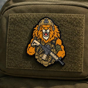 May include: A tactical morale patch featuring a stylized illustration of a roaring lion wearing a tan combat helmet and tactical vest, holding a black rifle. The patch is rendered in vibrant orange, tan, and black colors with a bold outline.