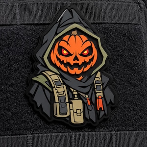 May include: A tactical morale patch featuring a stylized pumpkin-headed figure wearing a dark hooded cloak and tan utility gear. The character has glowing red eyes and a jagged, carved mouth, rendered in vibrant orange, black, and tan colors.