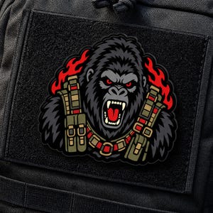 May include: A tactical morale patch featuring a snarling gorilla with red eyes and an open mouth, wearing olive green tactical gear with ammunition pouches. The design is set against a background of stylized red flames on a black base.